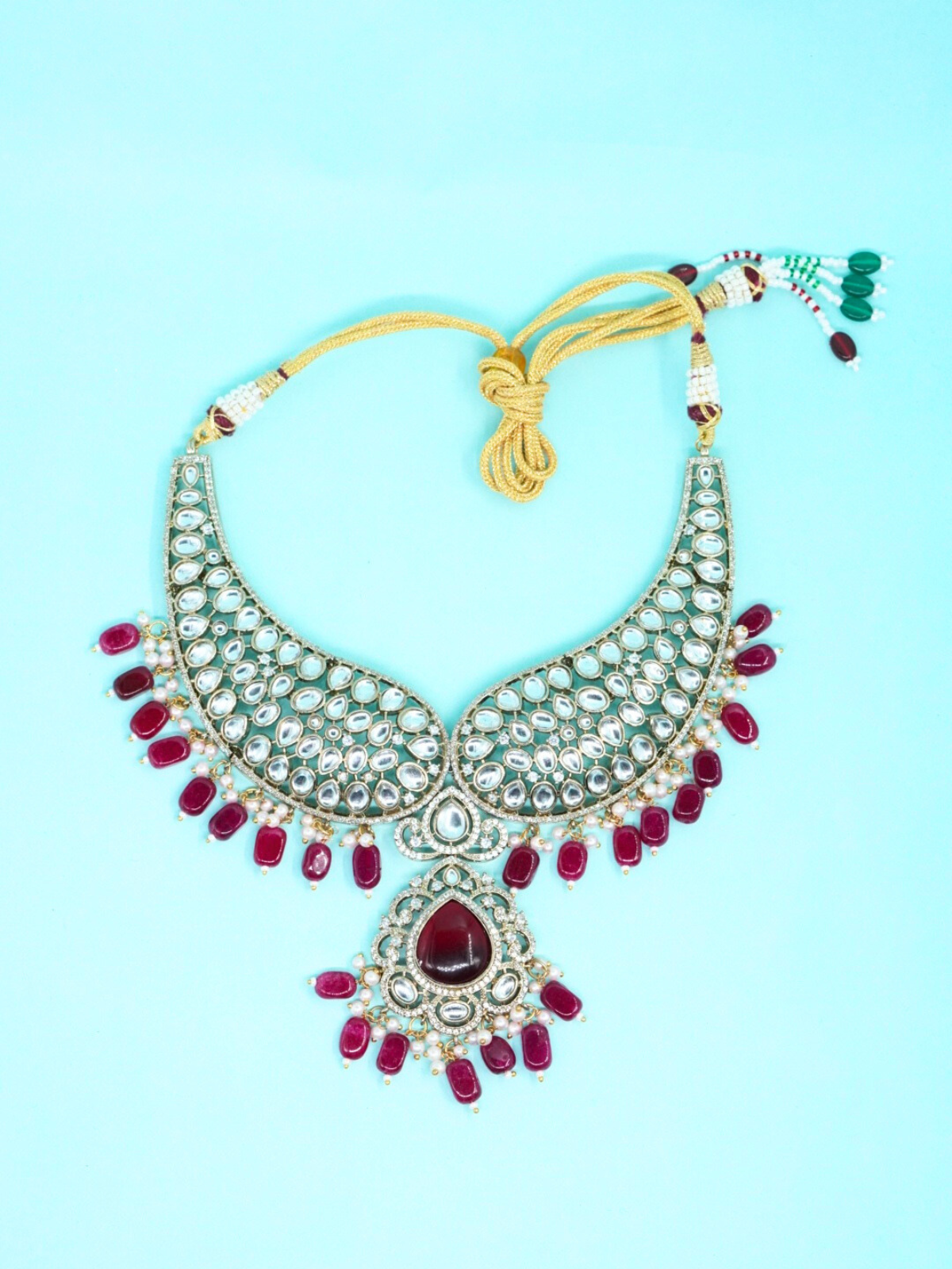 Bridal Kundan necklace set with red stone drops and gold tone finish on blue background