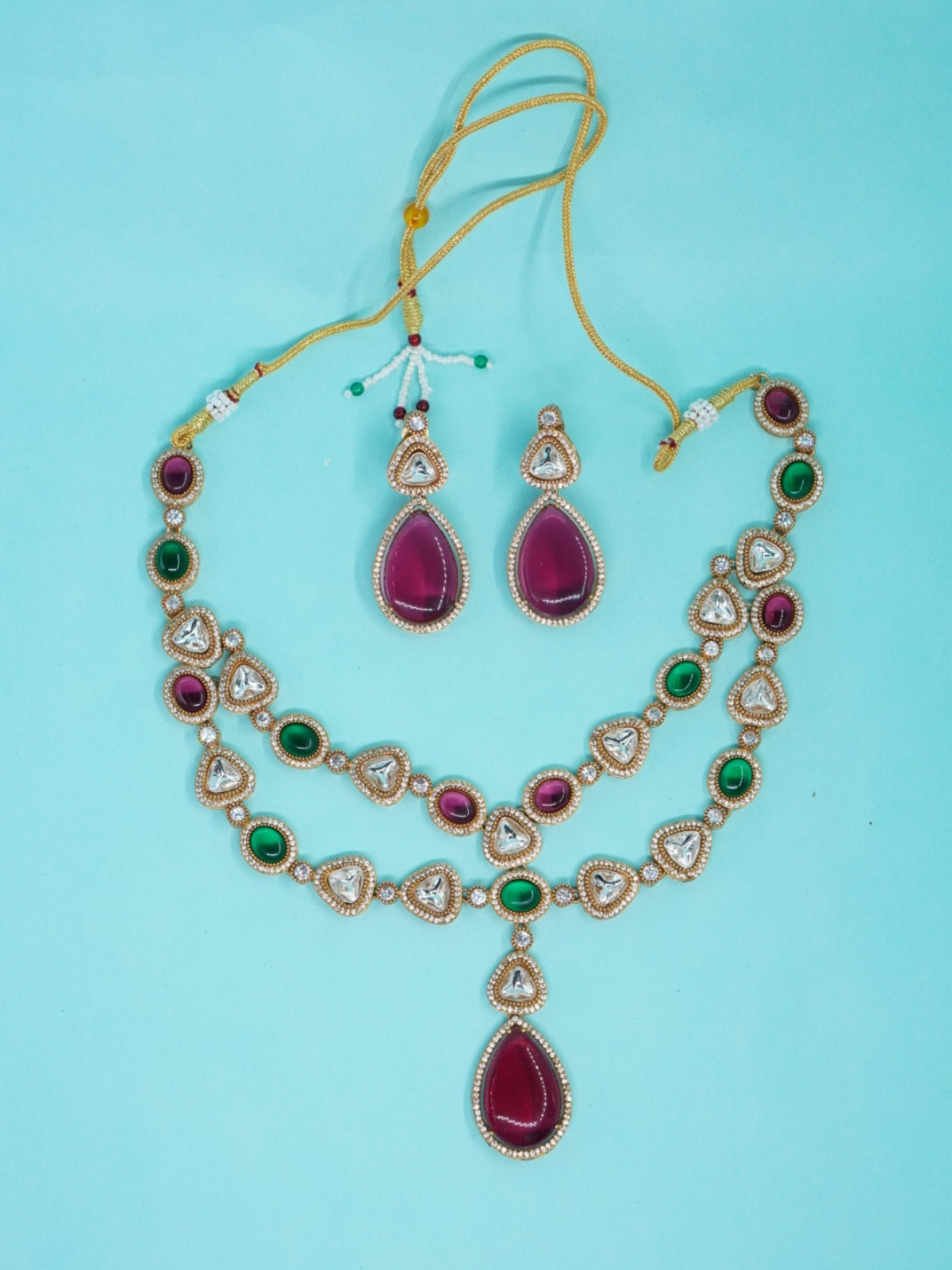Dual-tone kundan necklace set with green and pink stones, large pendant, and matching earrings on blue background