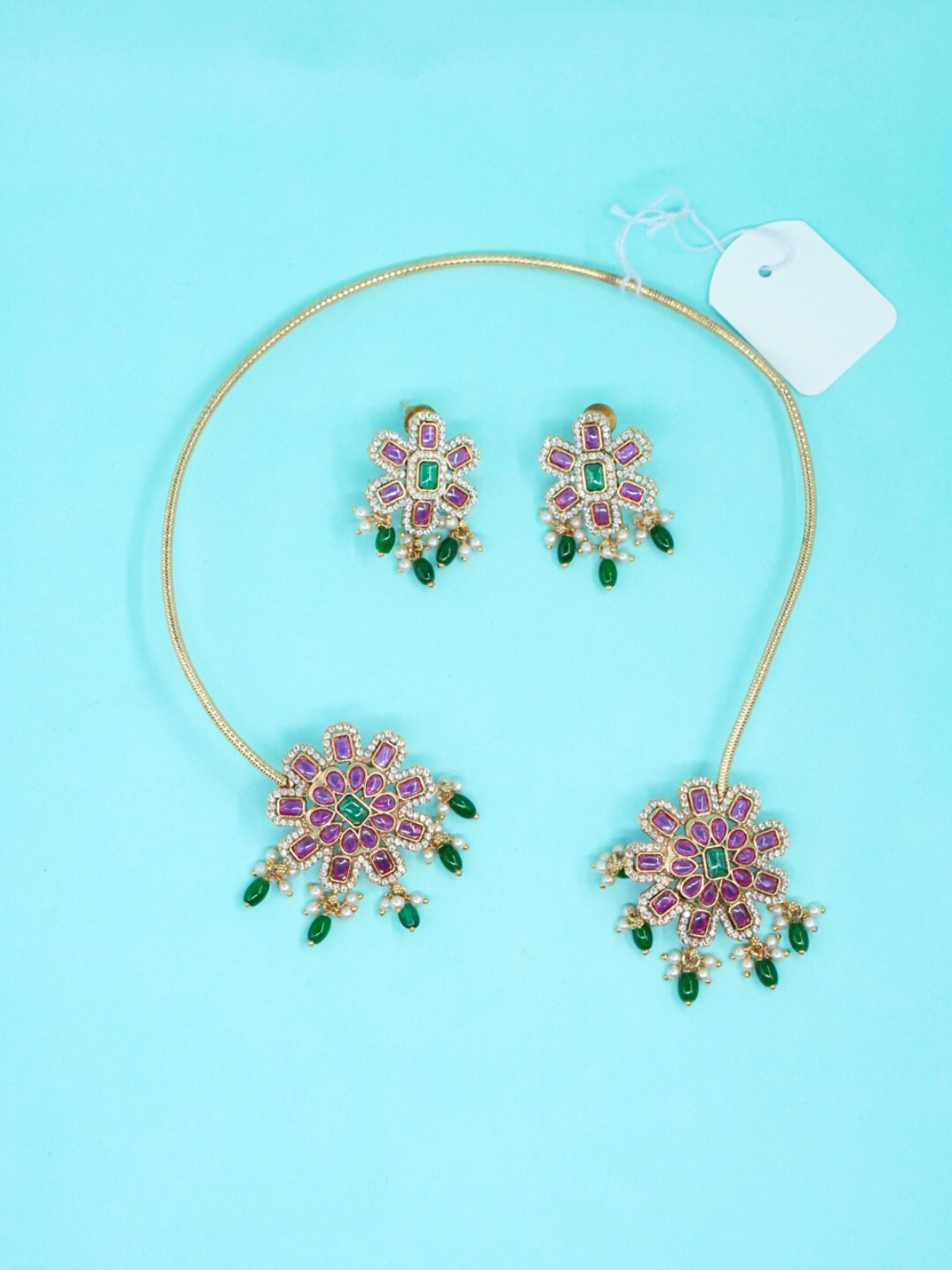 Short floral necklace set with pink and green stone work and matching earrings on copper base top view