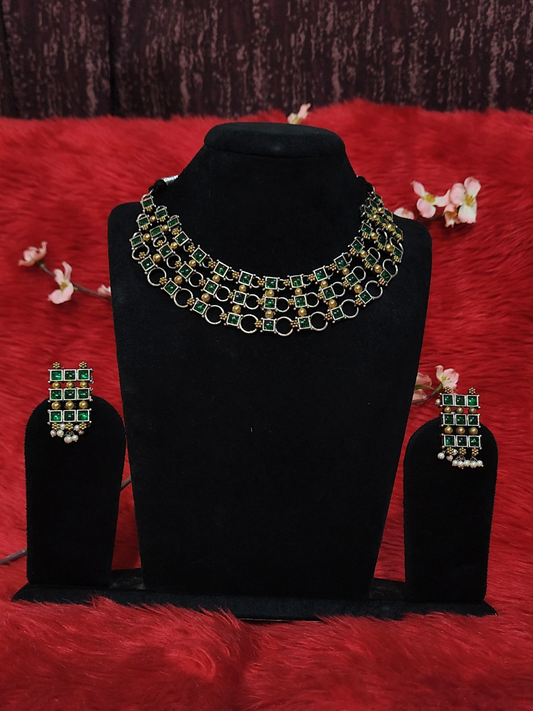 Silver replica choker necklace set with green stones and matching long drop earrings on black stand