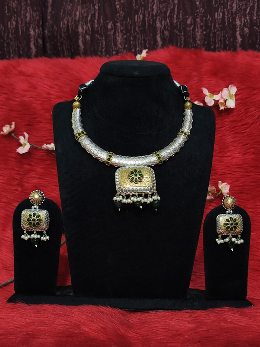 Silver replica necklace set with green and gold floral pendant and matching earrings on black stand 